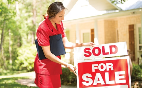 female real estate agent puts sold sign on home for sale sign; 10 reasons why you need a real estate agent