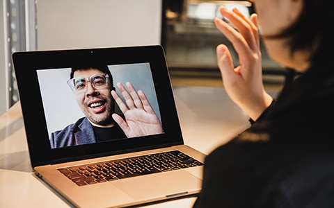 2 people having a virtual meeting via their laptop computers, waving at each other