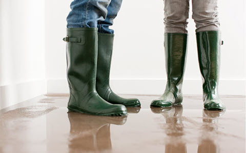 two people standing in a flooded room wearing rain boots