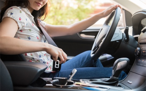 woman behind the wheel of her car putting her cell phone in the center console, 7 Common Car Accidents and How to Help Avoid Them