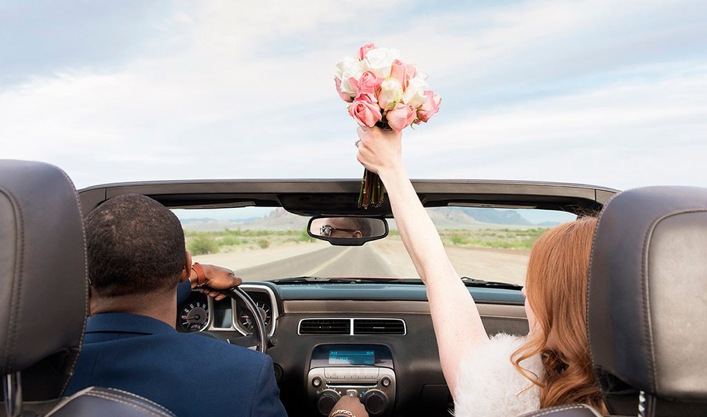 Husband and wife driving off in a convertible car after getting married