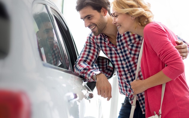Younger couple looking at new cars at car dealership