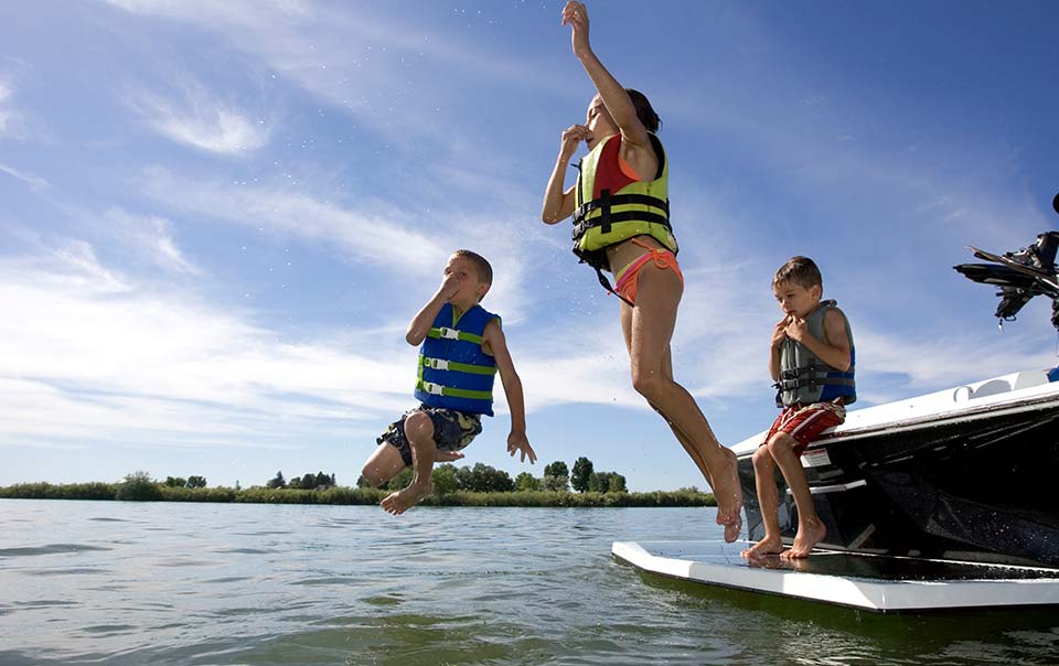 Three kids jumping into the water from a boat