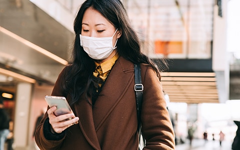woman outside wearing a face mask while looking at her phone