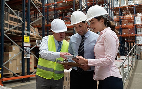 Warehouse employees, wearing a hardhat, holding clipboard and digital tablet