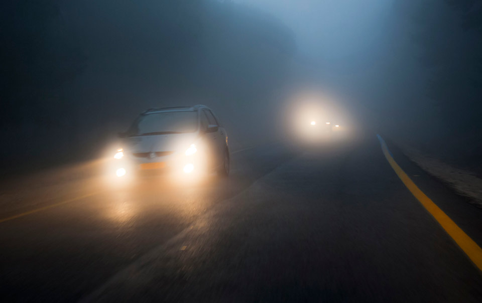 Car driving in fog at night with headlights on