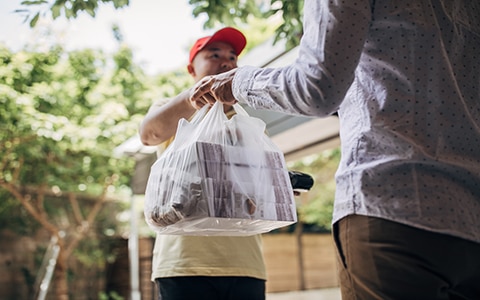 food delivery person handing over food to a man in his home, adapting your food service business to the pandemic
