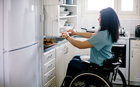 Woman in wheelchair pulling modified cabinet in her kitchen