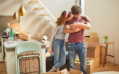 Couple inside home with moving boxes holding a baby-How Often Should I Review My Insurance Coverage?