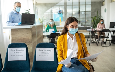 woman sitting in waiting room at clinic wearing a mask and gloves, How to Improve Employee Health, Wellness and Well Being