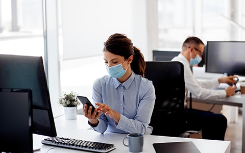 workers at their desks in the office who are wearing masks. How to Keep Your Employee Safe in the Workplace During COVID-19