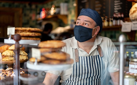 man in mask and apron standing behind bakery counter, How to Scale Products and Services to Increase Profitability