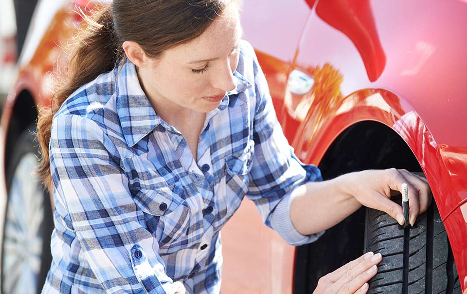 Woman checking tire tread of car as part of regular car maintenance routine