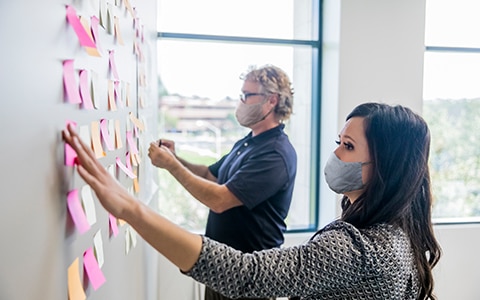 A man and a woman working to organize a wall of post it notes. Rethinking Roles Post-Pandemic
