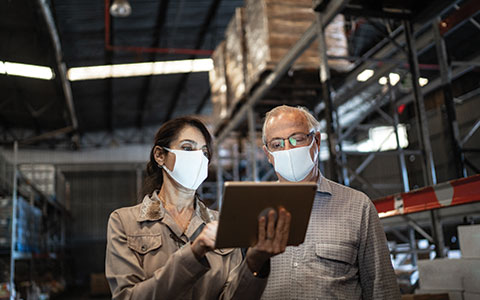 man and woman in masks looking at a tablet in a warehouse. The Right Business Insurance Coverage to Protect Your Company